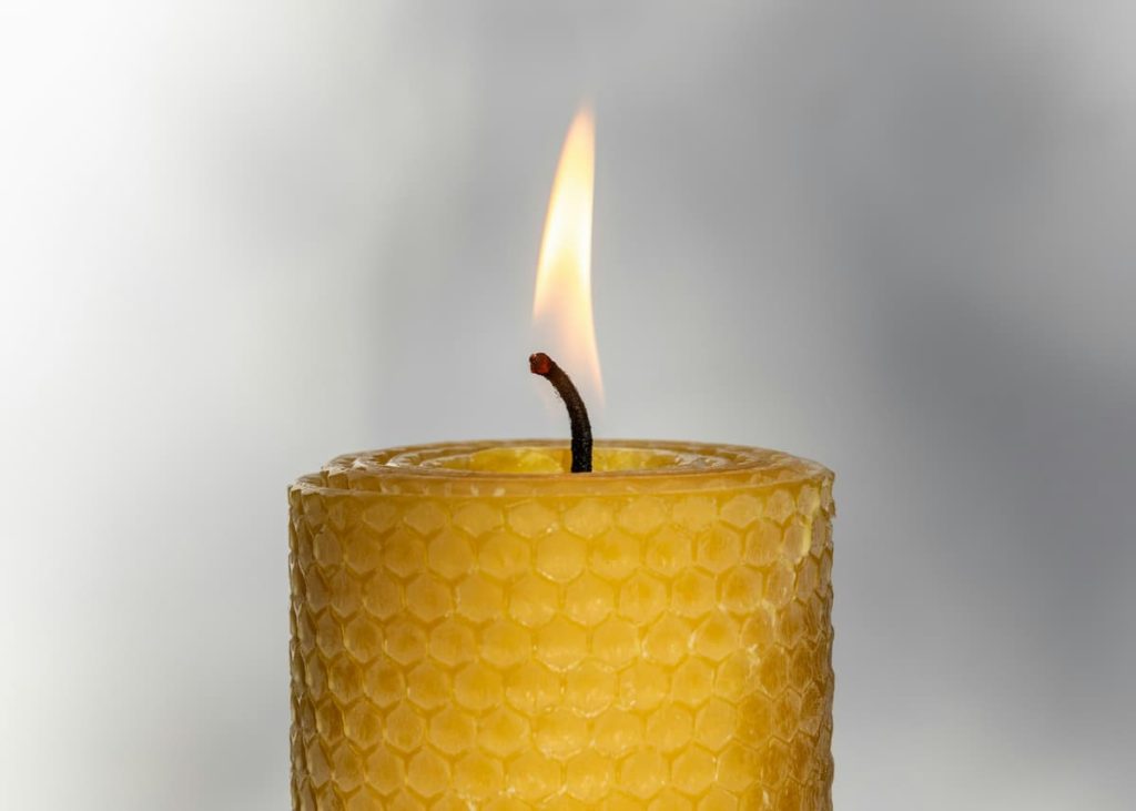 A lighted yellow beeswax candle showing the honeycomb shape.