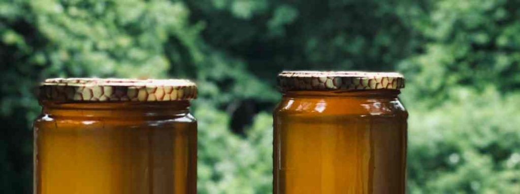 Two jars of honey with an unfocused background of trees