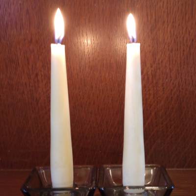 Two lit creamy white beeswax candles in glass holders on a wooden background